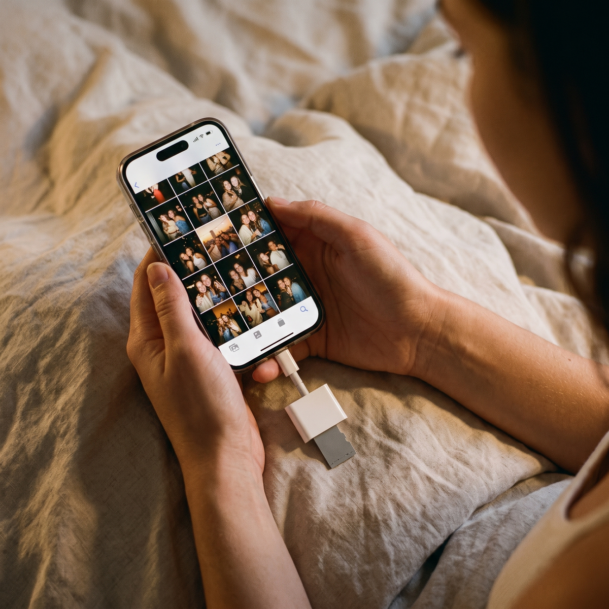 The Lightning memory card reader plugged into a phone, the screen showing a grid of warm night photos from the camera