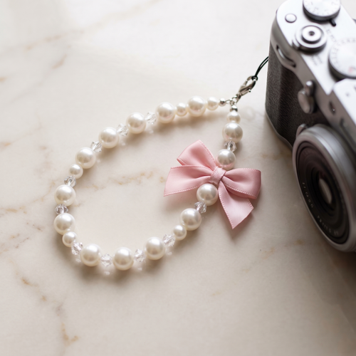Pink Bow pearl bead wrist strap with a soft pink satin bow charm on cream marble